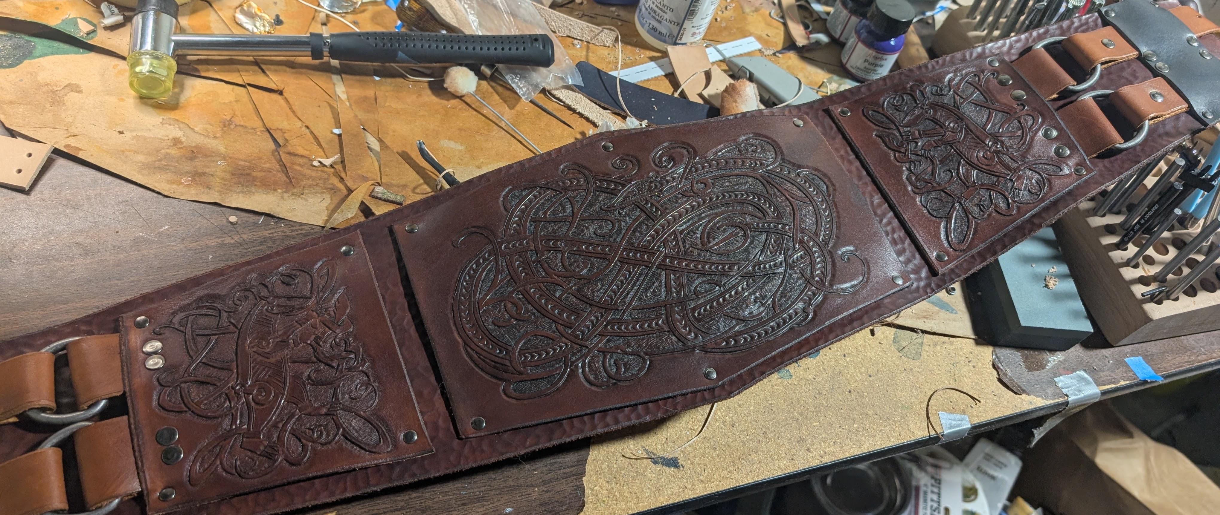 A brown leather kidney belt spread out on a workbench cluttered with tools.