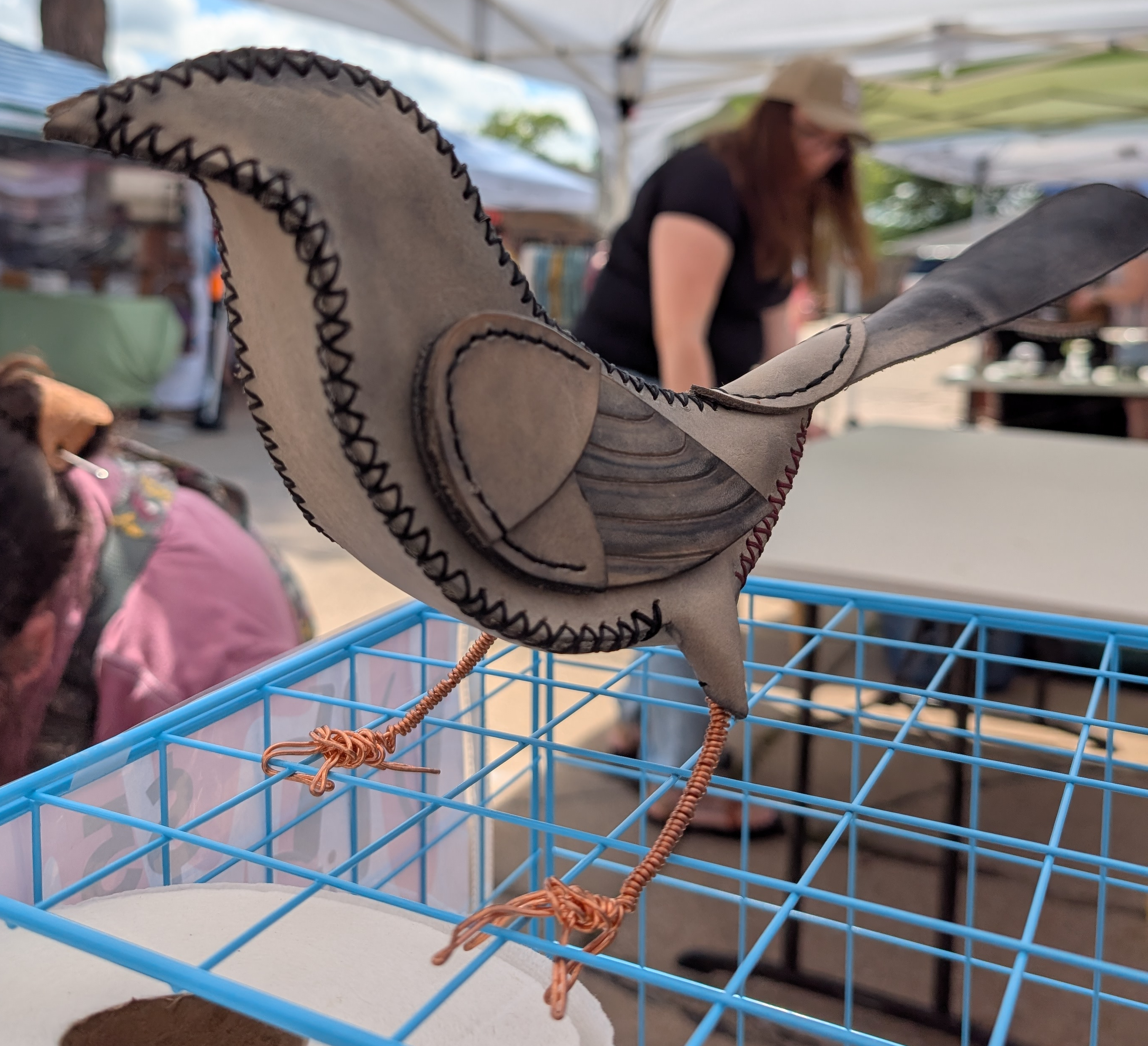 A stylized depiction of a gray catbird made of stitched leather