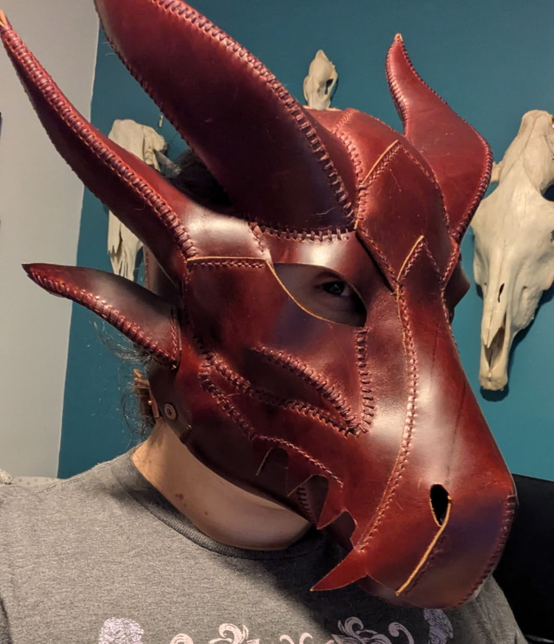 Person in a grey t-shirt wearing a full-face red leather mask in the shape of a dragon's head